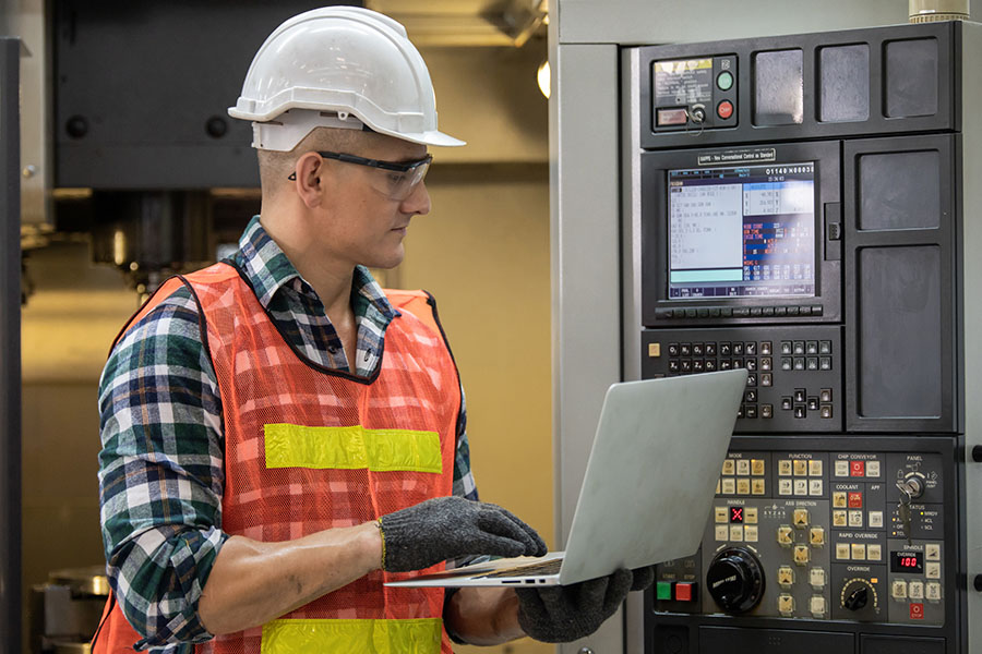 project manager operating machinery and laptop at precision machining company